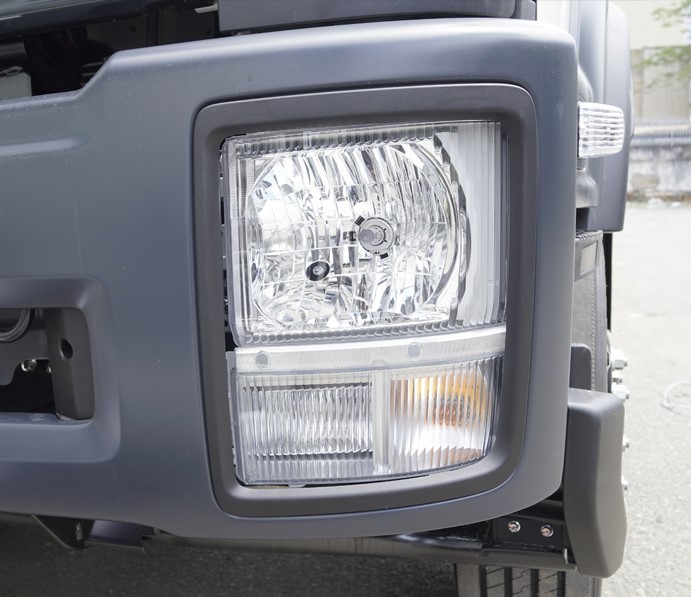 Cận cảnh cụm đèn pha Halogen trên xe tải Isuzu series F, tích hợp đèn pha và đèn xi nhan, tăng cường khả năng chiếu sáng và tín hiệu giao thông.