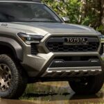 alt text: Lưới tản nhiệt hầm hố của xe bán tải Toyota Tacoma Trailhunter với logo Toyota màu vàng đồng và dải đèn LED phụ trợ.