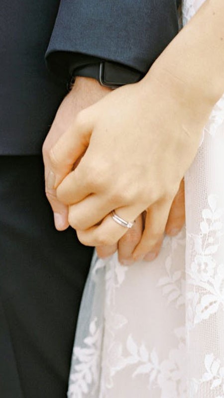 Cặp đôi nắm tay nhau trên con đường lãng mạn với hàng cây xanh, tạo nên không gian thơ mộng.