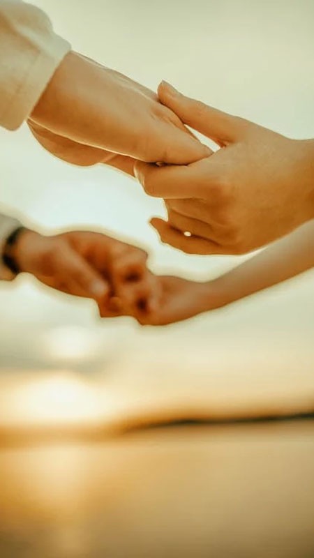 Cặp đôi nắm tay nhau đi dạo trên bờ biển lúc hoàng hôn, tạo nên khung cảnh lãng mạn và ấm áp.