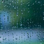 Mặt kính bị che phủ bởi những giọt mưa, làm mờ hình ảnh bên ngoài, thể hiện sự ảnh hưởng của mưa đến tầm nhìn