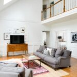 Phòng khách tươi sáng và thoáng đãng với tường trắng, sàn gỗ cứng, ghế sofa và ghế bành ấm cúng.