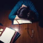 Một sinh viên với đầu gục xuống bàn, cảm thấy choáng ngợp với công việc.